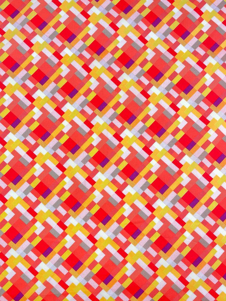 The Printed Poplin - Jigsaw - 112cm by Super Cheap Fabrics showcases a vibrant geometric design with intersecting diamonds in red, yellow, orange, pink, and white. The symmetrical pattern creates an optical illusion of depth and overlap.